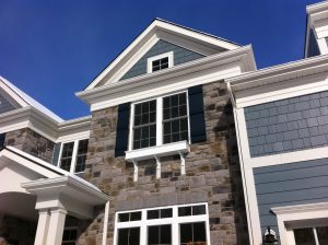 The exterior siding of a custom home. There is stone and blue siding.