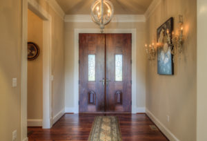 A foyer with candlelight lamps, large brown double doors, and beautiful hardwood flooring.