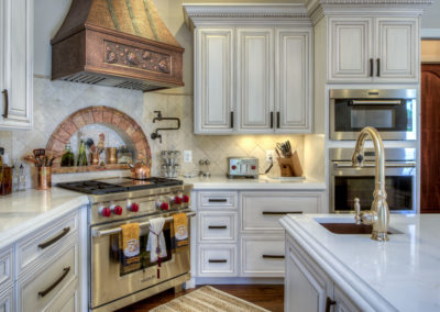 A white and tan accented kitchen with a sink, pot filler, gas stove, and oven.