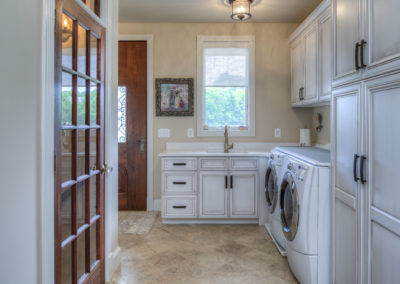 A glass and wood door opens into a white and tan laundry room with a sink, washer, and dryer.