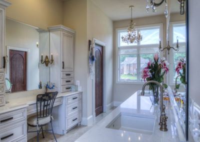 A bathroom suite with white granite counters, a small chandelier, two sinks, and a vanity with room to sit. Custom shelves surround the vanity.