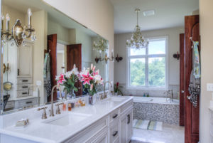 A custom bathroom with white granite counters, a mosaic style bathtub, and a chandelier.