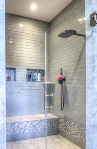 A custom built shower with blue-grey tile, mosaic style accents, built-in room for shower products.