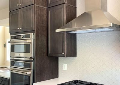 A custom built kitchen a white backsplash, dark brown cabinets, a double oven, and luxury gas stove.