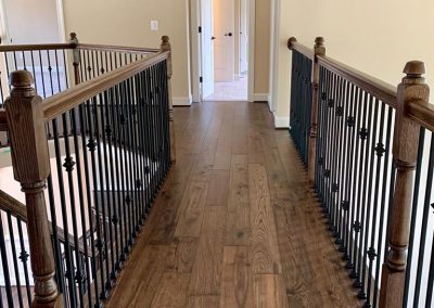 Open second floor hallway with brown hardwood flooring, black and