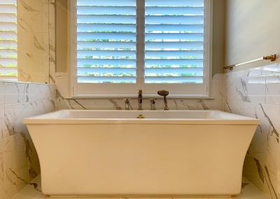 A large white bathtub with a window above. There is a shower head attached next to the faucet.