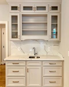 White marble wet bar with white and glass cabinets.