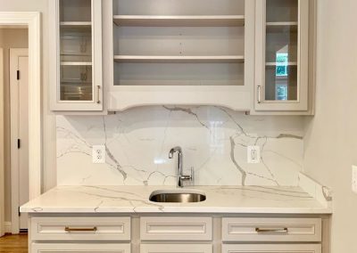 White marble wet bar with white and glass cabinets.
