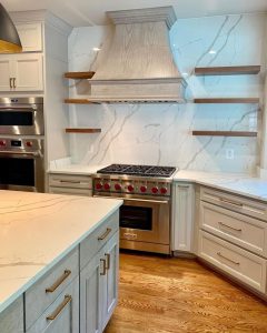 White marble and grey wood kitchen with a gas stove and hood vent.