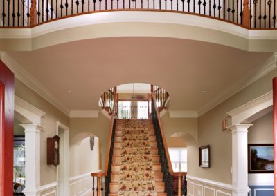 An open door shows you the foyer of this home, with a grand staircase leading up to the open second floor hallway. The stairs are brown with carpet treading.