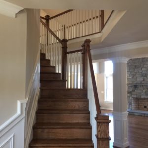 A brown hardwood staircase leading up to an open second floor hallway. There is a stone fireplace and pillar in the background.