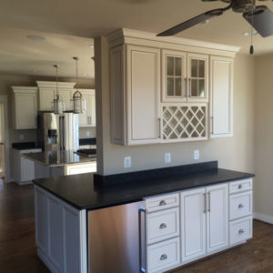 A kitchen in the background, a dry bar with stainless steel mini fridge and white cabinets.