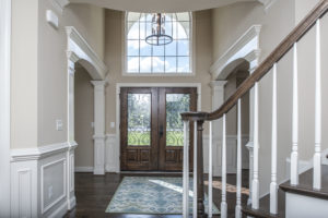 An open foyer with cream white walls, dark brown hardwood floors and door.