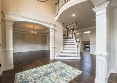 A white and dark brown staircase, open foyer, dining room and living room can be seen in the back.